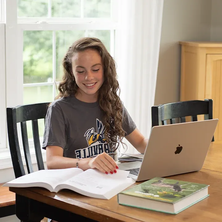 High school student studying with laptop and books at kitchen table